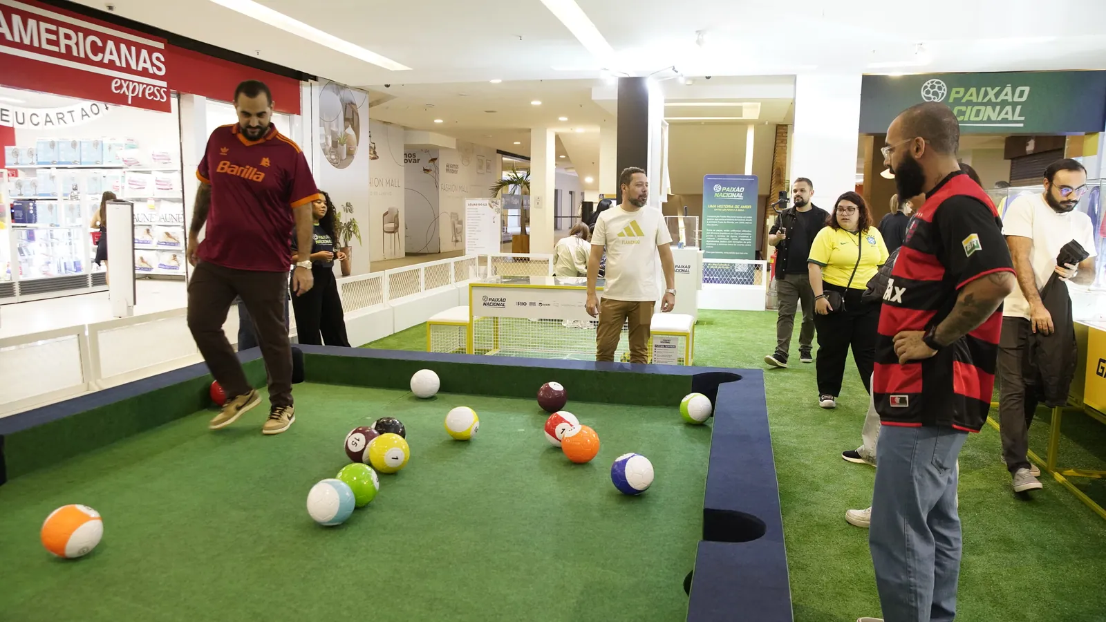 Público jogando na mesa de sinuca de bola de futebol da Exposição Paixão Nacional