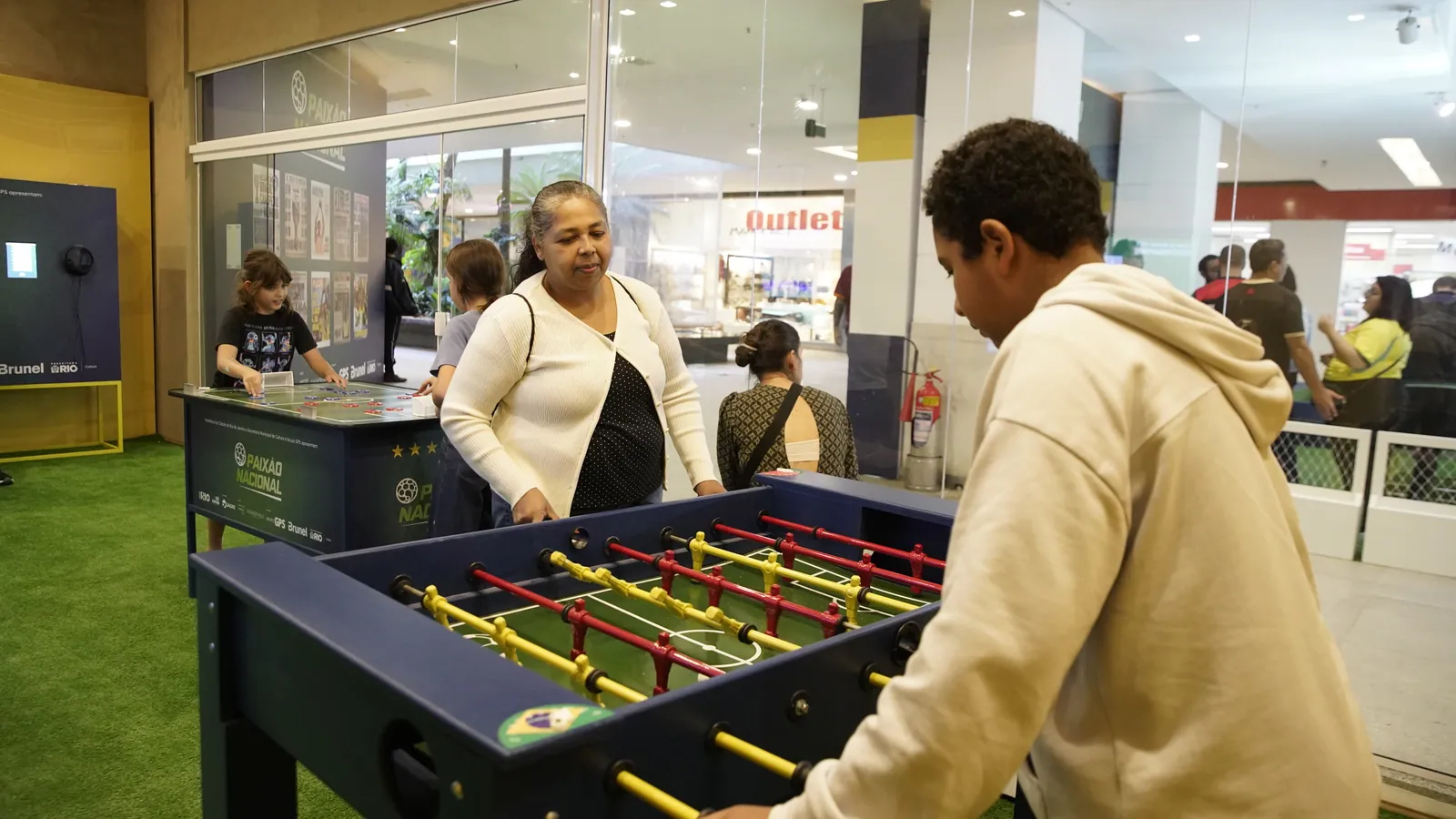 Visitantes jogando pebolim na área interativa da Exposição Paixão Nacional