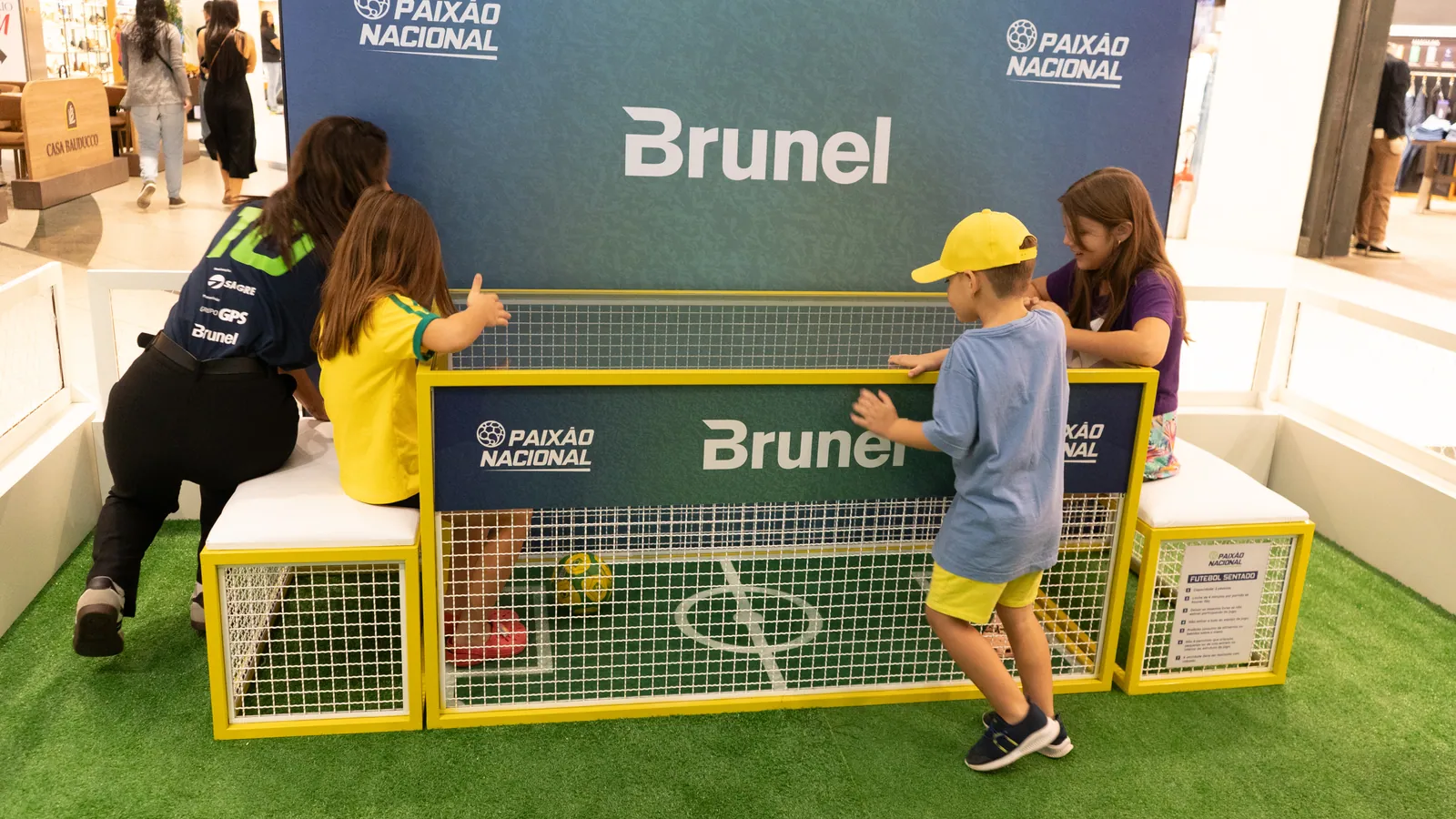 Crianças com camisa da seleção interagindo com as vitrines da Exposição Paixão Nacional